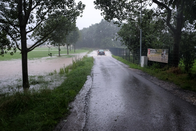 Ein Auto überquehrt eine überflutete Straße.